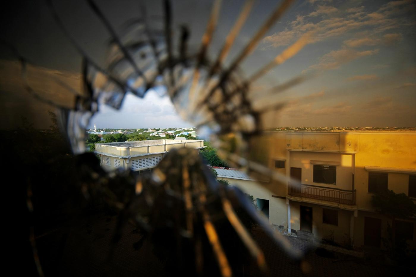 Bullet hole in glass window photographed from the inside of a building. Through the hole, you can see a concrete bulding in an urban landscape,