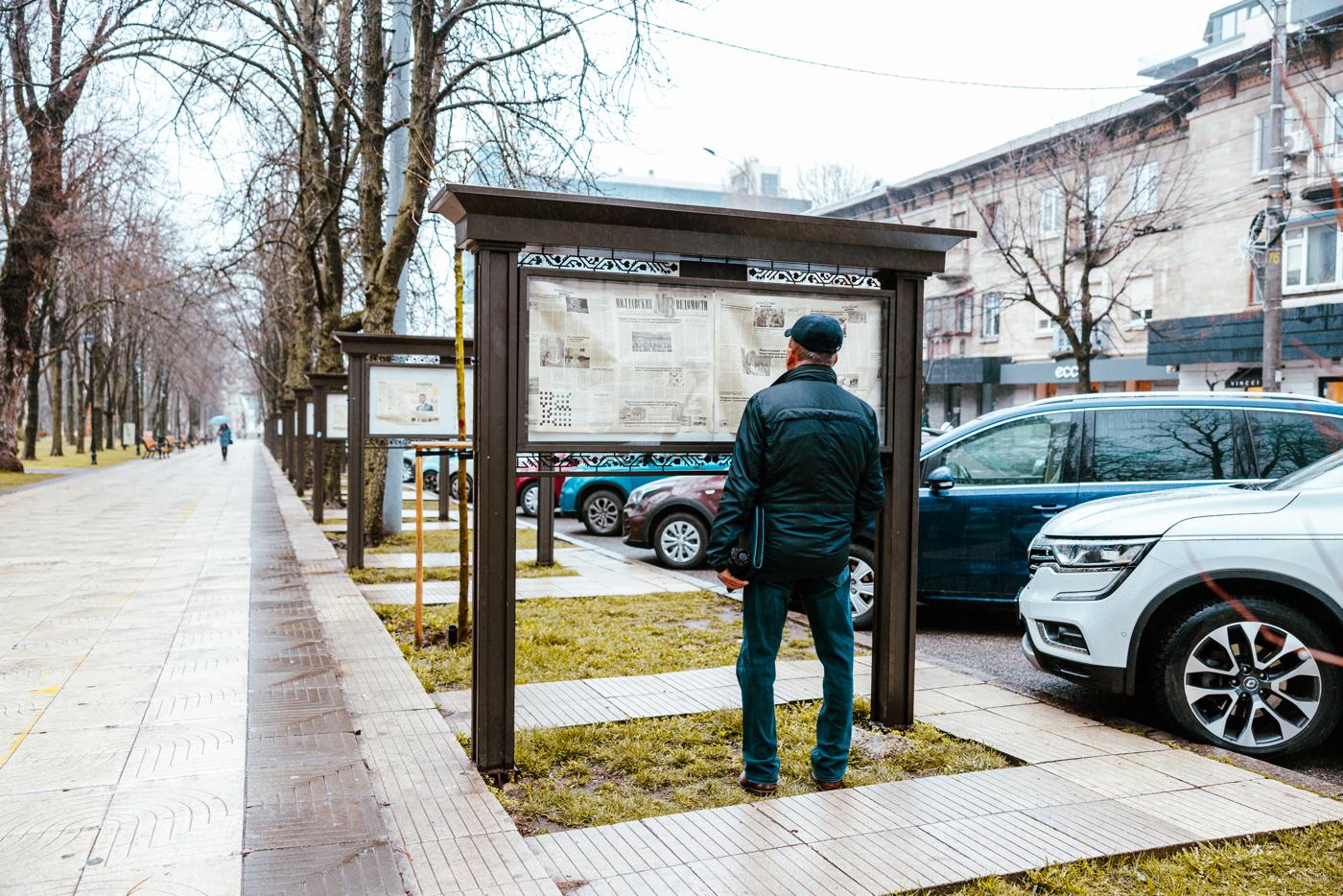En man står med ryggen mot kameran och läser en tidning uppsatt i en av flera inglasade anslagstavlor längs en allé i Chisinau, Moldaviens huvudstad.
